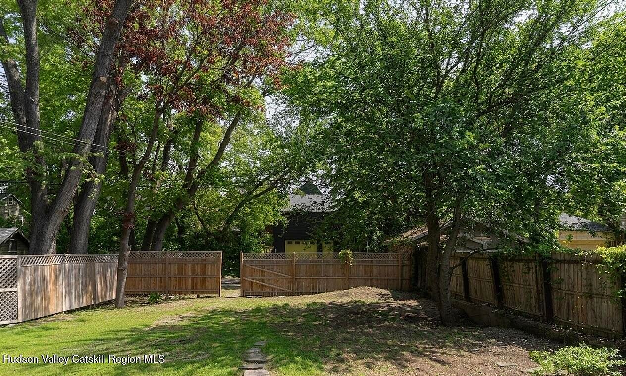Private fenced rear garden behind the three Federal townhouses with mature shade canopy, deep lawn, and a reserved parking pad at the far gate. 516-518 State Street, Hudson, New York